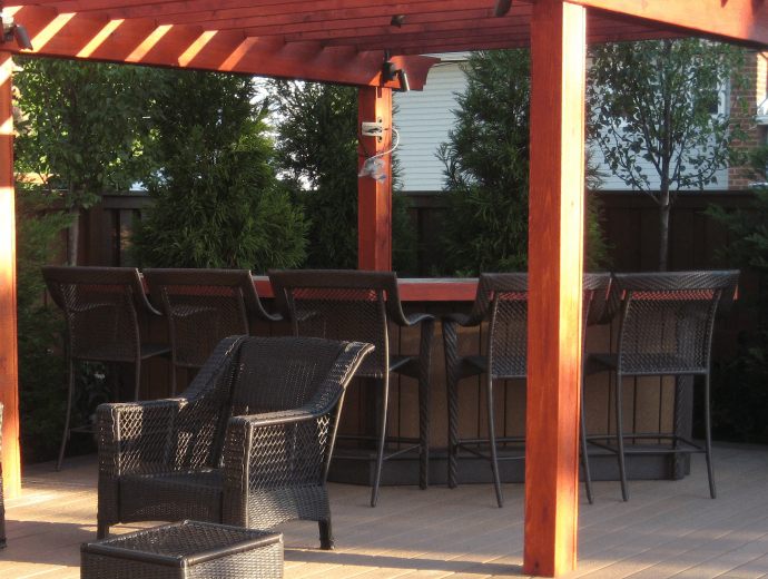 Outdoor kitchen with stunning red pergola, black mesh chairs, and lush greenery